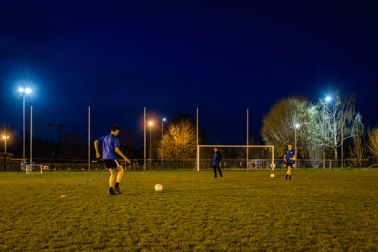 Voetballers trainen op een veld dat 's avonds verlicht wordt door schijnwerpers.