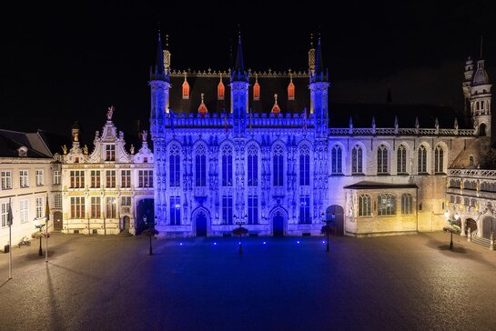  Stadhuis in Brugge, sfeervol verlicht op de Grote Markt bij avond.