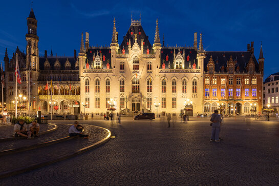 Stadhuis in Brugge, sfeervol verlicht op de Grote Markt bij avond.