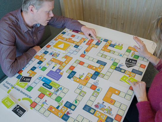 Beleef de klantreis van een gedropte elektriciteitsklant op een interactieve en speelse manier. Een foto van mensen die het bordspel Klantreis aan het spelen zijn