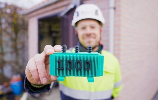 Medewerker toont een miniatuurtransformator met het cijfer 1000 als symbool voor de mijlpaal in transformatorverzwaringen.