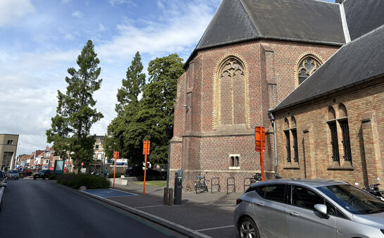 Hoe creëer je draagvlak voor publieke laadpunten? Publieke laadpaal in open ruimte bij kerk met geparkeerde wagens in Roeselare.