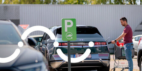 Man plugt laadkabel in elektrische wagen op de parking van een supermarkt