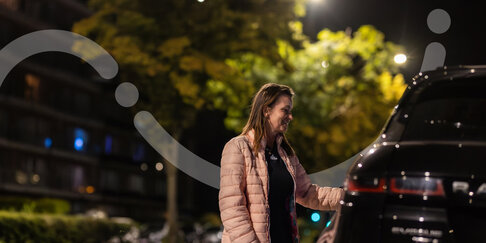 Persoon in een verlichte straat bij een geparkeerde auto, als illustratie van tijdelijke interactieve straatverlichting.